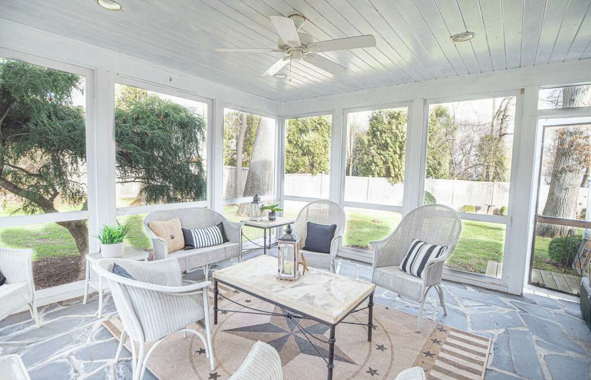 Enclosed screened porch at 139 Northwood Road, Fairfield. A paving stone pathway bisects the carpet of green front lawn dotted with shaped shrubbery as it leads to the entrance of the white house with black shutters and distinctive gable hip roof. The pale blue door opens into the center hall foyer, where there is a gracefully curved spiral staircase to the second floor. This house offers 2,710 square feet of living space. Unlike most houses of this vintage there is no formal living room. Instead, it has a sizable family room with a wood-burning fireplace, French doors to the large deck and backyard and a door to a large, screened porch. The porch has a slate floor and a ceiling fan.
