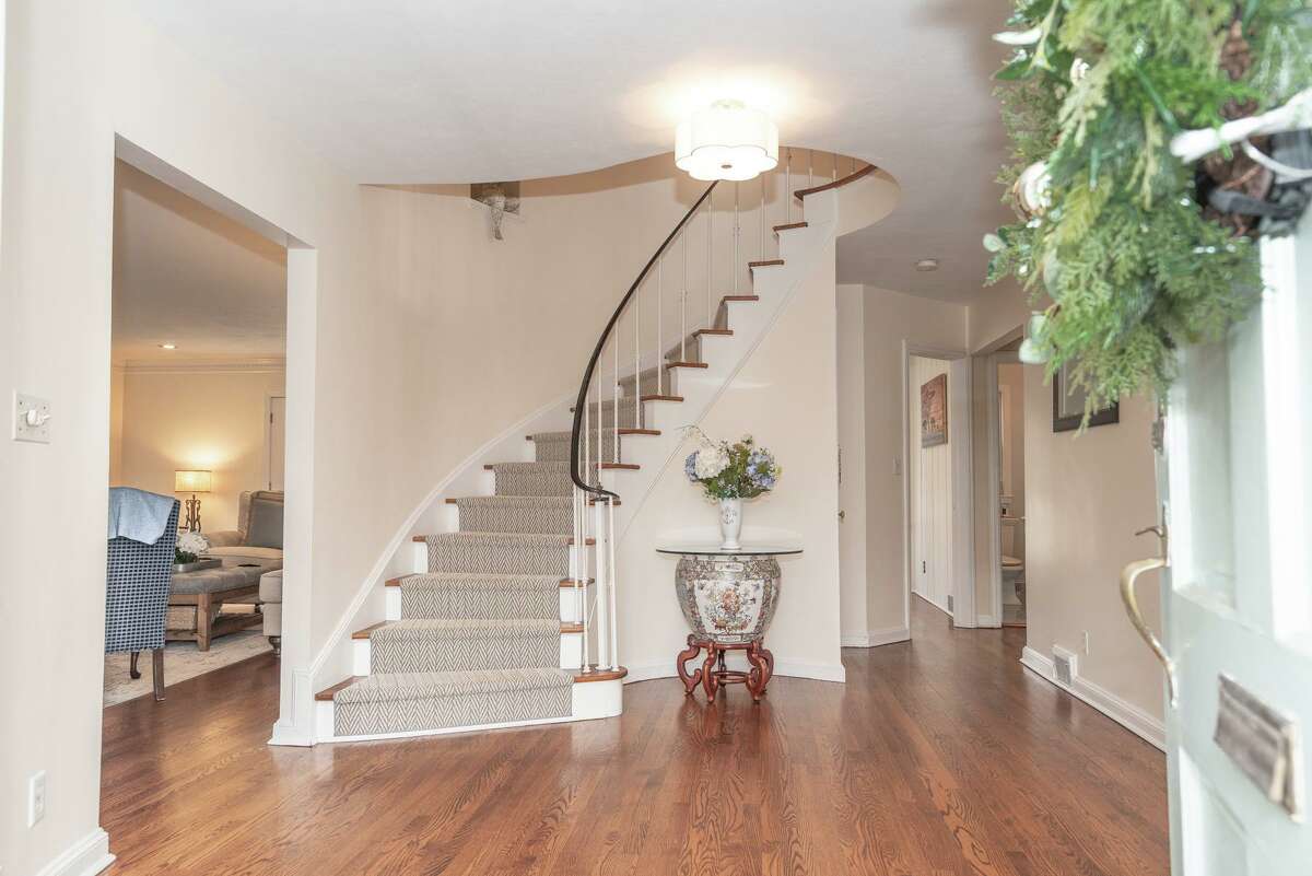 Graceful spiral staircase in the foyer at 139 Northwood Road, Fairfield. The formal dining room features chair railing, two built-in corner china cabinets, and dentil crown molding. A café-style door leads into the updated chef’s kitchen with a two-tiered center island/breakfast bar, granite counters, and high-end appliances. On the first floor there is also a half bath, and a flexible use room that could serve as a den, home office, a media room or play room. This room has wood-paneled walls, built-in bookshelves, ceiling fan and French doors to the deck.