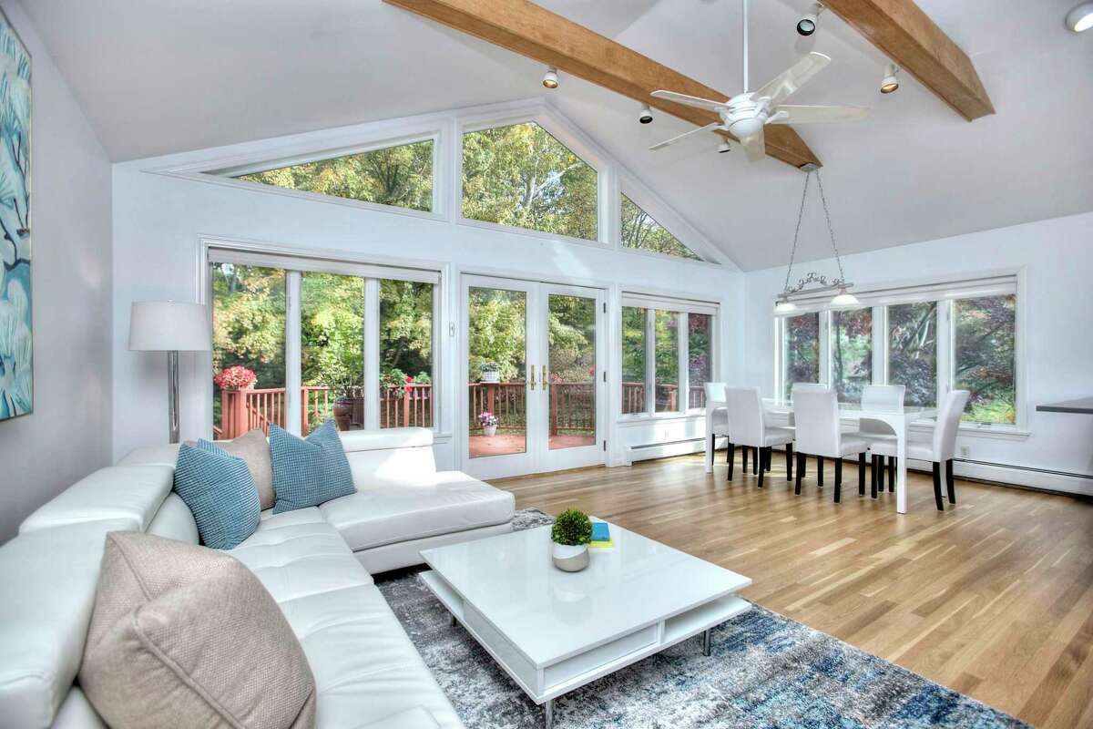 The great room at 6 Peaceful Lane, Westport has French doors to the deck. It was built in 1962 but improvements throughout the years, including many recent updates, have provided this 10-room house with many modern conveniences including a newer, designer eat-in kitchen with quartz countertops, an extraordinarily large and bright walk-out lower level with recreation space, and an open floor plan. A carpet of green grass and pachysandra comprises the front lawn, and a tall maple tree stands near the entrance. The front door is flanked by sidelights and a tall transom, which combine with numerous windows to allow an abundant flow of natural light into this house.