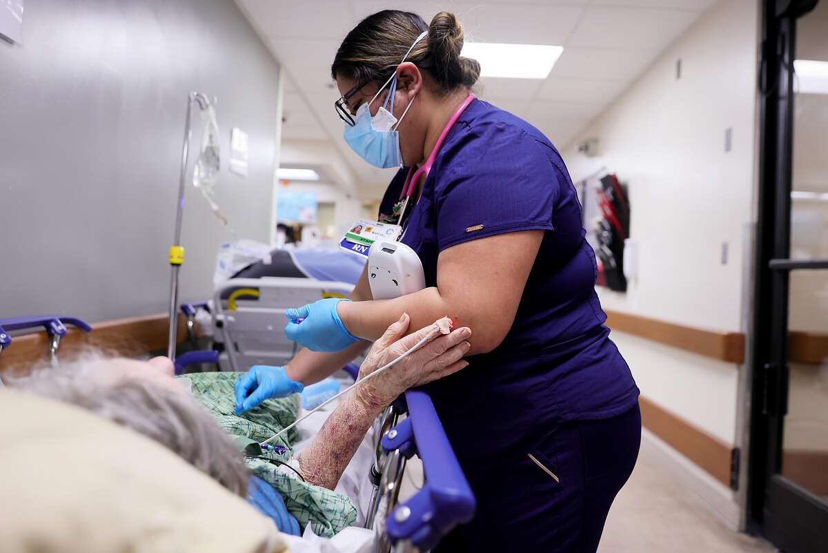 APPLE VALLEY, CALIFORNIA - JANUARY 05: A registered nurse cares for a patient on a stretcher in a hallway of the overloaded Emergency Room at Providence St. Mary Medical Center amid a surge in COVID-19 patients in Southern California on January 5, 2021 in Apple Valley, California. California has issued a new directive ordering hospitals with space to accept patients from other hospitals which have run out of ICU beds due to the coronavirus pandemic. The order could result in patients being shipped from Southern California to Northern California. (Photo by Mario Tama/Getty Images)