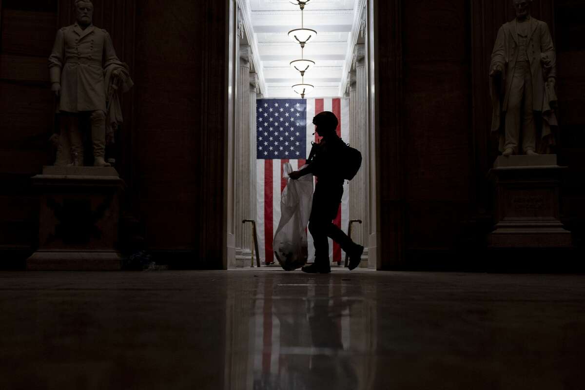 An ATF police officer cleans up debris and personal belongings strewn across the floor of the Rotunda in the early morning hours of Thursday, Jan. 7, 2021, after protesters stormed the Capitol in Washington, on Wednesday. (AP Photo/Andrew Harnik)