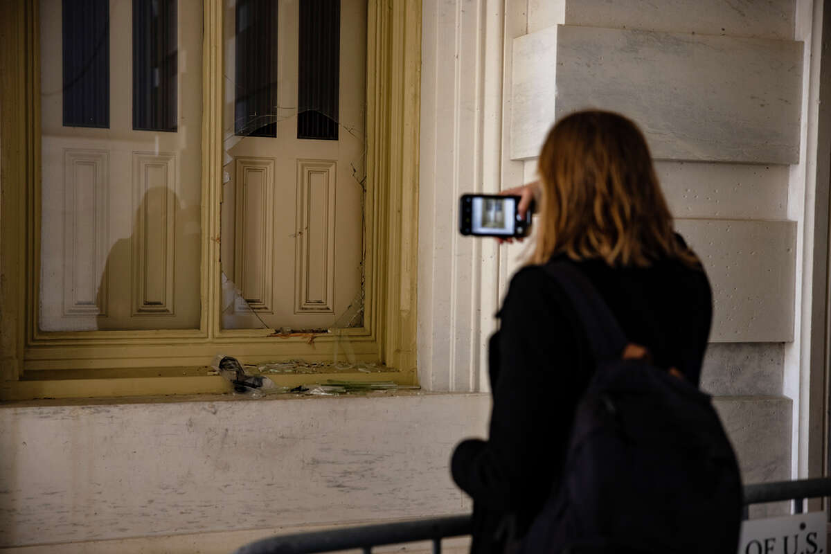 A woman takes a photograph of a shattered window next to the Senate Carriage Entrance on the eastern side of the U.S. Capitol building on January 7, 2021 in Washington, DC. Following a rally yesterday with President Donald Trump on the National Mall, a pro-Trump mob stormed and broke into the U.S. Capitol building causing a Joint Session of Congress to delay the certification of President-elect Joe Biden's victory over President Trump.