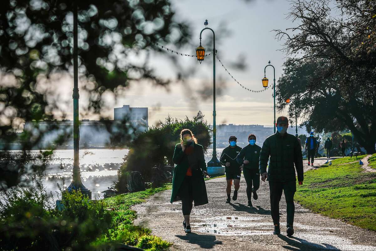 Masked walkers explore Oakland’s Lake Merritt. The Bay Area has reported an average of 4,400 COVID cases a day this week.