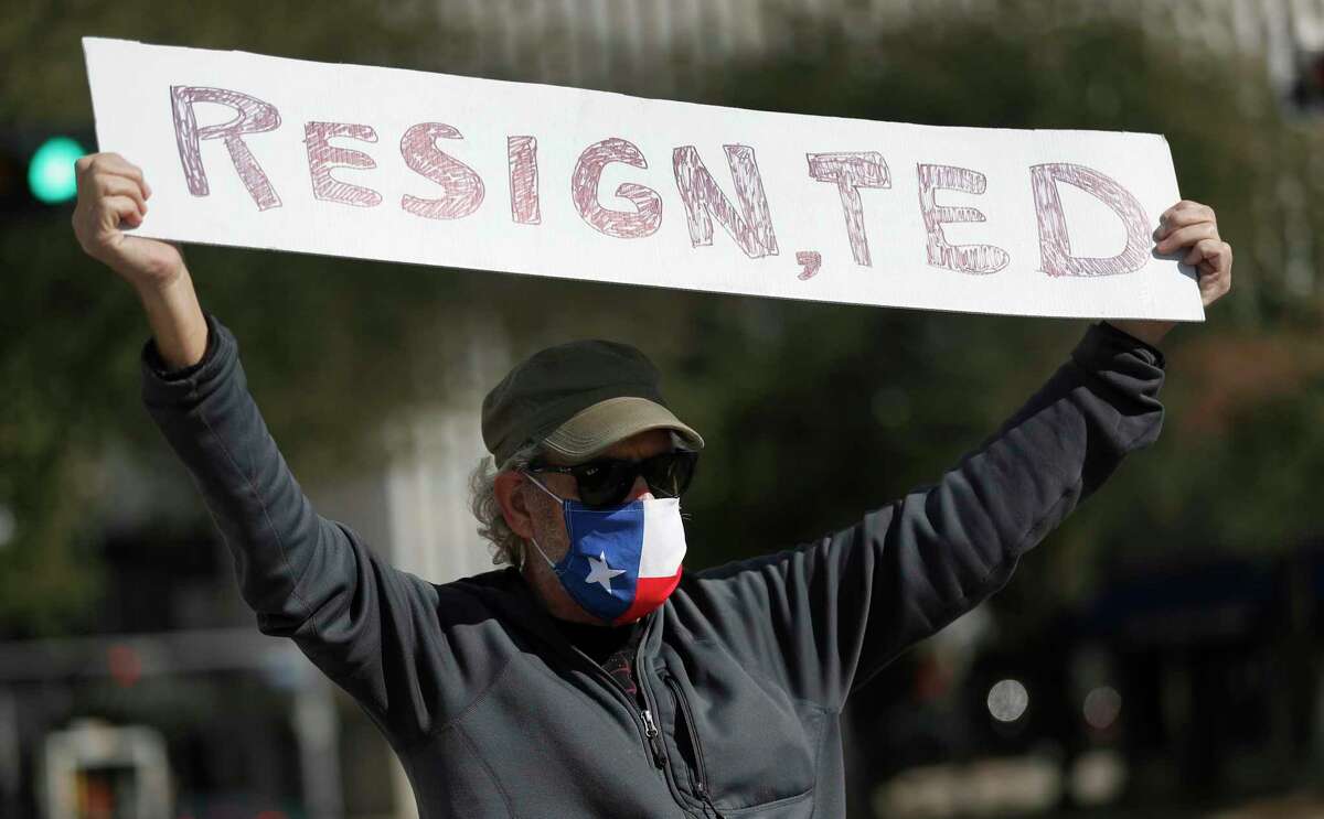 A protester wearing a Texas flag mask holds up a sign reading “Resign, Tex” as Houston activists call for Senator Ted Cruz to resign at the Leland Federal Building,Thursday, Jan. 7, 2021, in Houston.