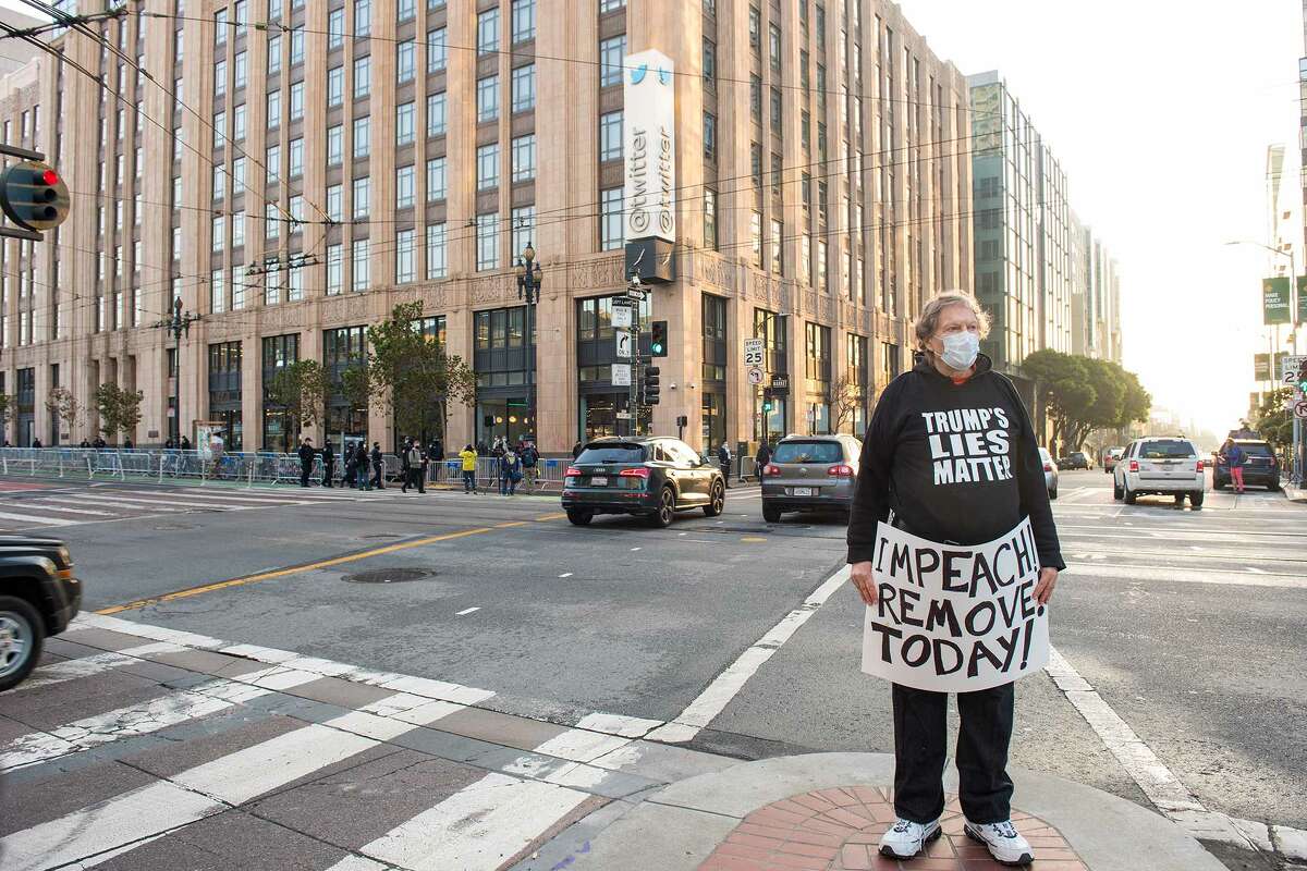 A man carries a sign across the street from the Twitter headquarters on Monday, January 11, 2021.