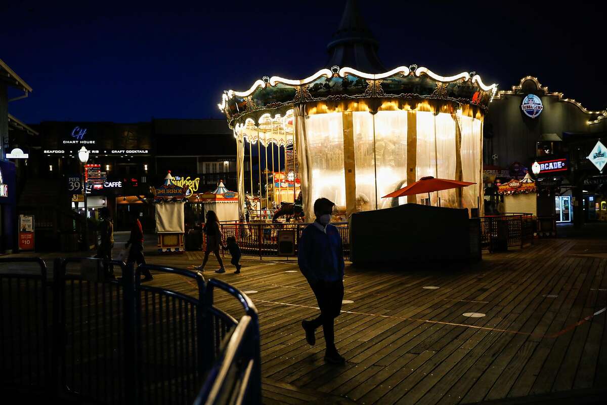 Tourists pass by the carousel at Pier 39 at dusk on Wednesday, Nov. 25, 2020 in San Francisco, California. Despite a surge in COVID-19 cases hundreds of tourists came to visit Pier 39.