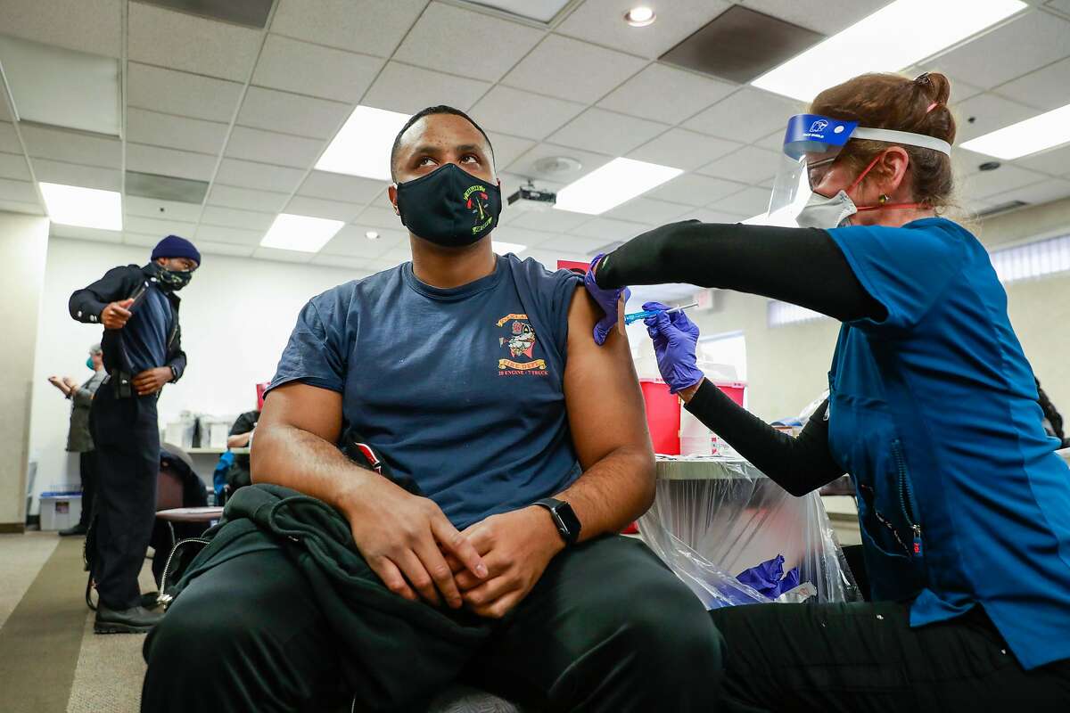 Mario Jones (left), with the Oakland Fire Department, gets his second dosage of the Pfizer vaccine from nurse Virginia Barrett (right) at St. Rose Hospital on Wednesday, Jan. 6, 2021 in Hayward, California. They were administering both the first dosage and second dosage of the vaccine.