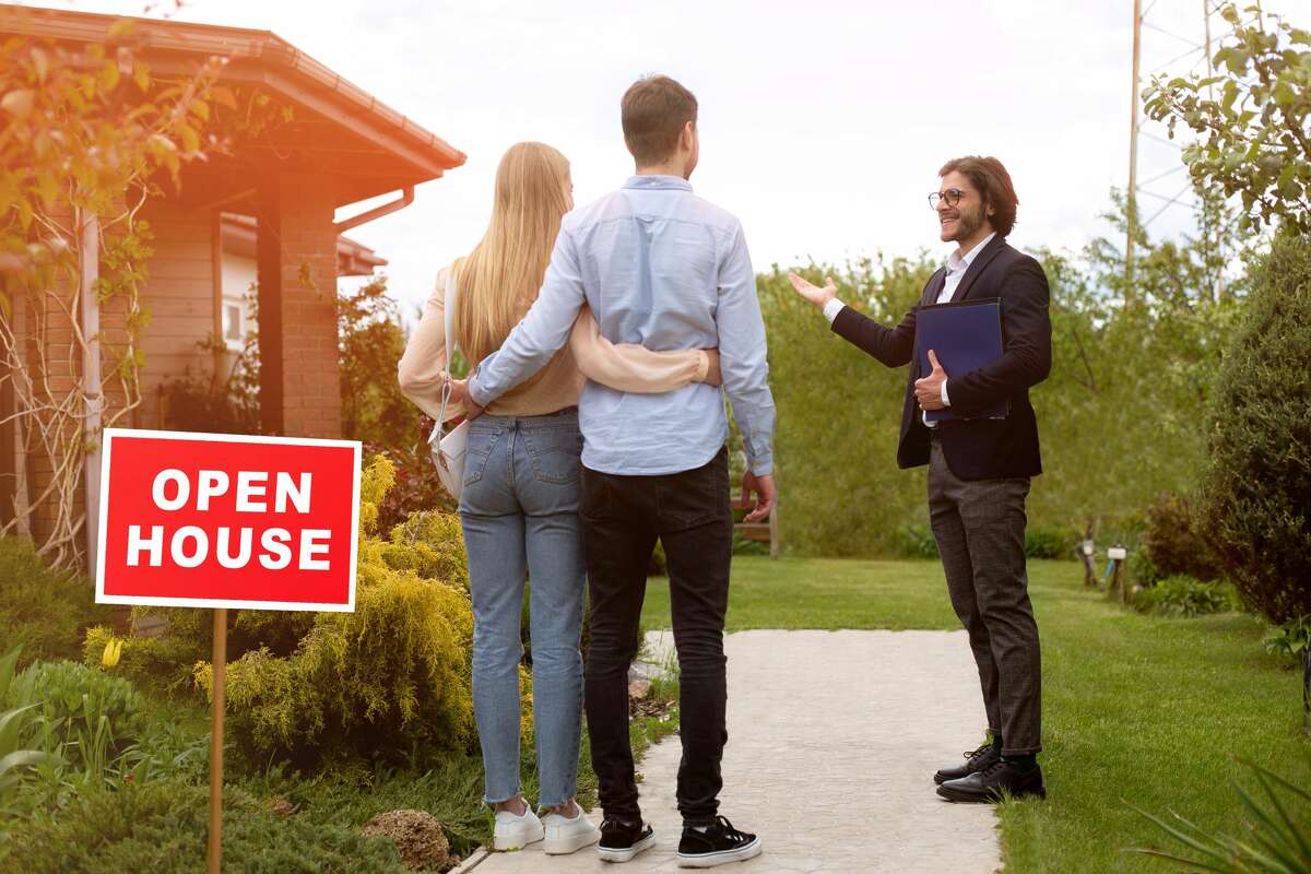 Confident real estate manager showing open house to young couple outdoors