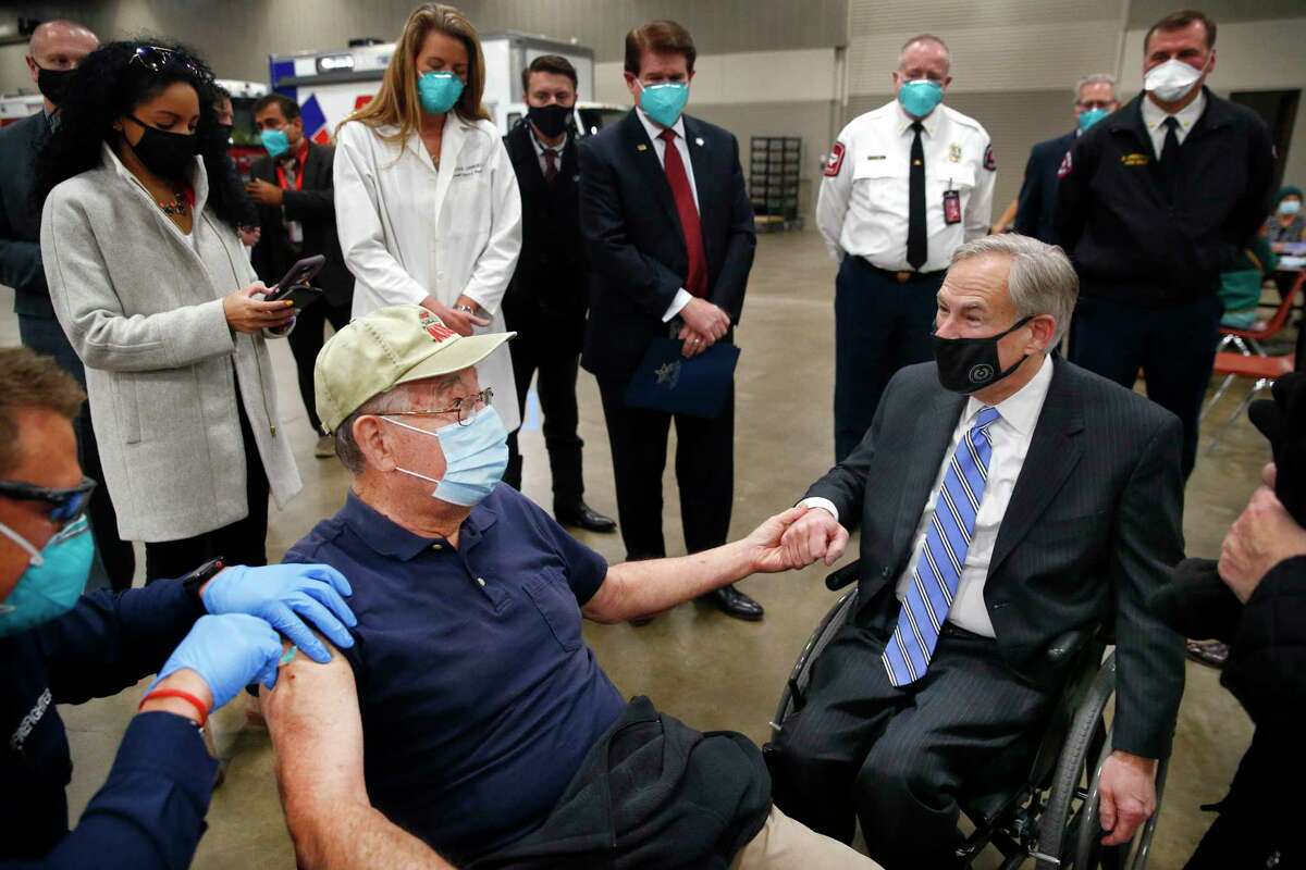 Texas Governor Greg Abbott, right, holds the hand of 86 yr-old Al Godfrey of Arlington as he receives his COVID-19 shot at a mass vaccination site inside Esports Stadium Arlington & Expo Center in Arlington, Texas, Monday, Jan. 11, 2021. Earlier Abbott met with local and state officials for a briefing and then provided an update on COVID-19 vaccine efforts in Texas. (Tom Fox/The Dallas Morning News via AP, Pool)