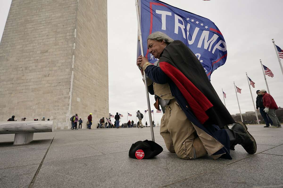 A man dressed as George Washington kneels and prays near the Washington Monument with a Trump flag on Jan. 6.
