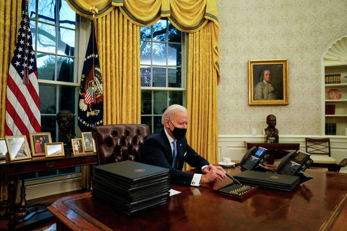 President Biden picks up a pen in the Oval Office to sign a raft of executive orders, including one that repealed his predecessor's Muslim travel ban, on Jan. 20.