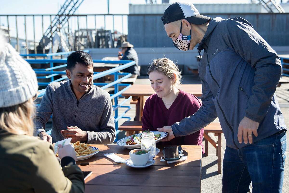 Juan Carlos serves Keshav Saharia of San Francisco (left) and Katie Donick of New York their lunch at the outside patio at Fish restaurant in Sausalito, one of the first places to reopen for outdoor dining after Gov. Gavin Newsom allowed it.