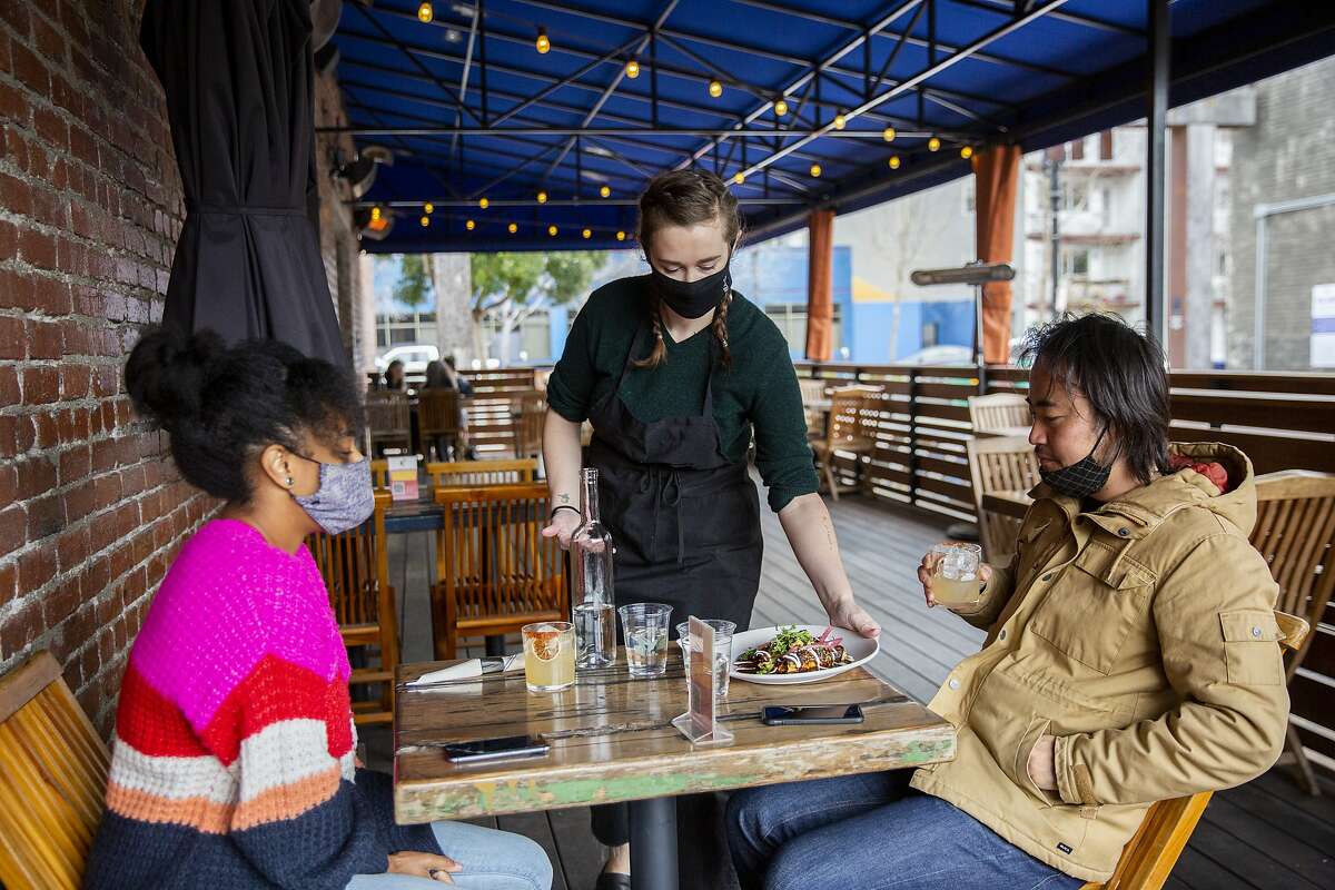 Maddie McGraw serves customers Rachel Kigano (left) and Ryohei Hinokuma at the Calavera patio on Tuesday, Jan. 26, 2021, in Oakland, Calif. The restaurant is open for takeout and outdoor dining.