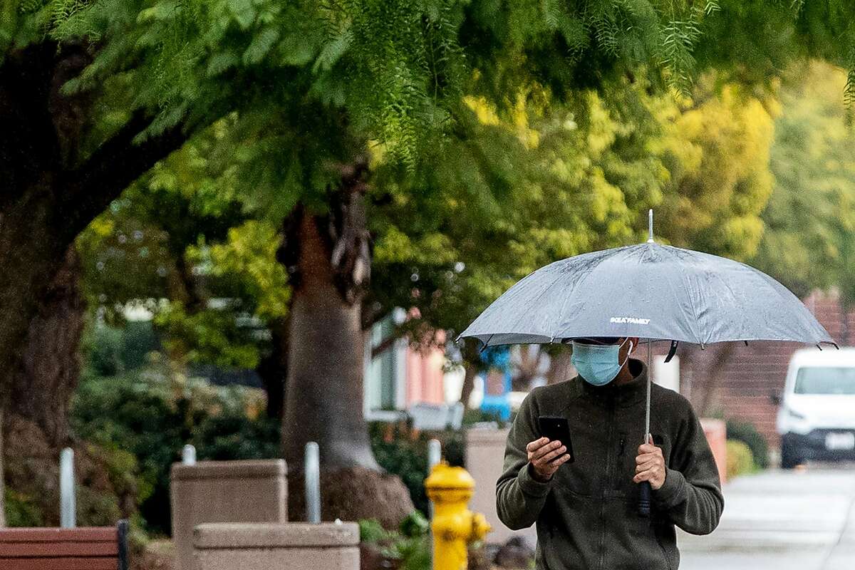 A person wears a mask while carrying an umbrella during a walk through San Jose State University's campus as rain falls in San Jose, Calif. Friday, January 22, 2021. Scattered showers are expected to soak the Bay Area Friday ahead of a series of storms predicted next week.