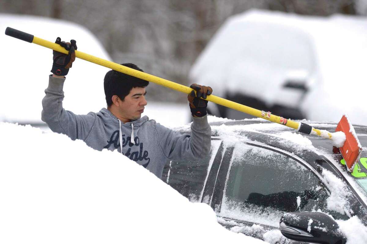 Angel Rodriguez, of Danbury, cleans the snow off of one of over two dozen cars and trucks on the Alves Auto Sales lot on Wednesday morning, January 27, 2021, in New Milford, Conn.
