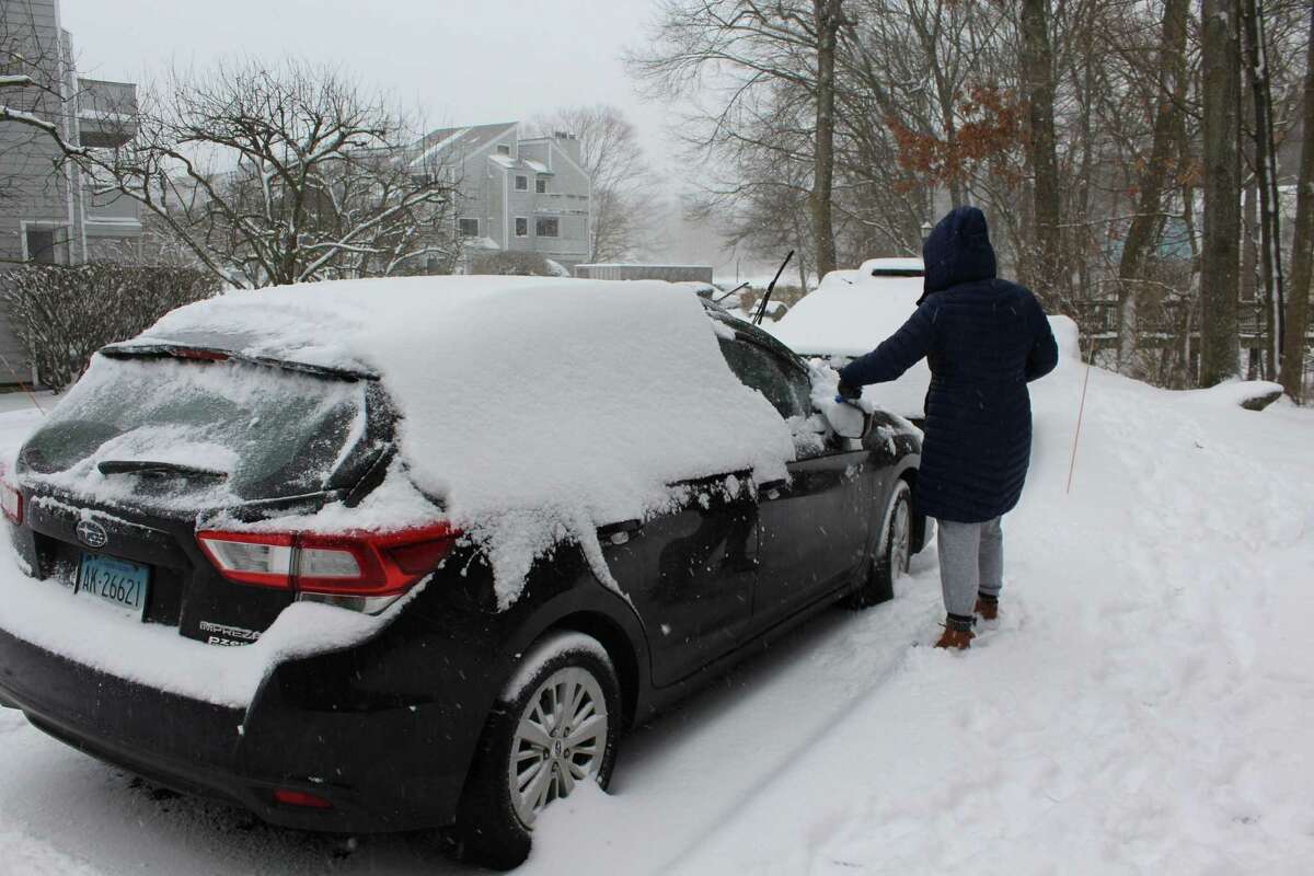 A Norwalk resident cleans off their car during a snow storm Monday, Feb. 1, 2021.