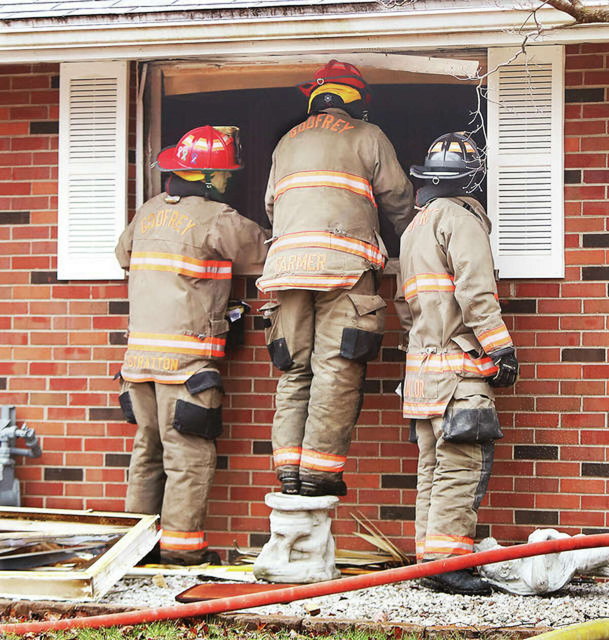 Godfrey firefighters stand and stare through a broken out window into a house Monday morning in the 2300 block of Wedgewood Avenue after extinguishing a fire at that brick home. Firefighters were watching as Illinois State Police Crime Scene investigators and others processed the scene inside where two people were found dead.