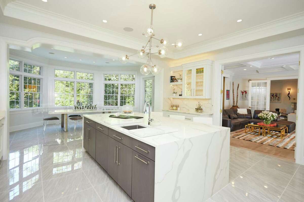 Spacious gourmet kitchen at 17 Woodway Lane, Westport. The cavernous, state-of-the-art gourmet kitchen features a long center island/breakfast bar with a waterfall counter, radiantly heated porcelain tile flooring, under cabinet lighting, a butler's pantry, a large breakfast nook, and high-end appliances including refrigerator drawers and a range with a pot-filler above it. The sizable and sunny home office features built-in bookshelves behind glass doors. Several areas, including the living and family rooms have doors to the patio and backyard, which features an outdoor kitchen.