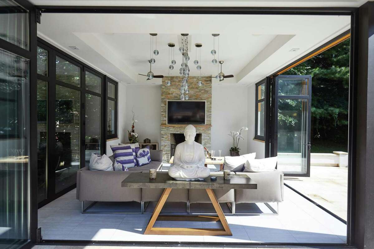 Glass house with fireplace and accordion doors at 17 Woodway Lane, Westport. For those who prefer yoga and meditation, this peaceful property features a waterfall wall and a unique modernist glass house with a wood-burning stone fireplace and three walls of accordion glass doors that open to bring the outside in. Enhancing the peaceful setting is the sight of the West Branch of the Saugatuck River, which wends its way through the lower portion of the property, close enough to enjoy the view, far enough to prevent fear of flooding. The owners of this house cross through a graceful stone arch to reach the riverbank.