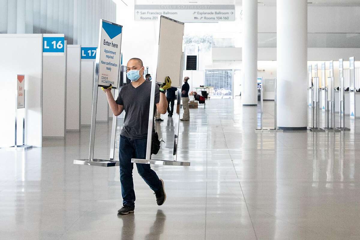 A city worker moves signage while working to prepare a mass COVID-19 vaccination site at Moscone South in San Francisco.