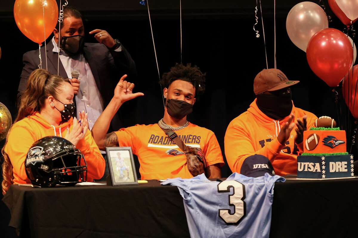 Harlan High School wide receiver Dre Spriggs flashes the "Birds up!" sign after signing with UTSA beside his parents, Erica and Shalaby Spriggs, and coach Eddie Salas, rear, during a ceremony in the school's auditorium on Wednesday, Feb. 3, 2021.