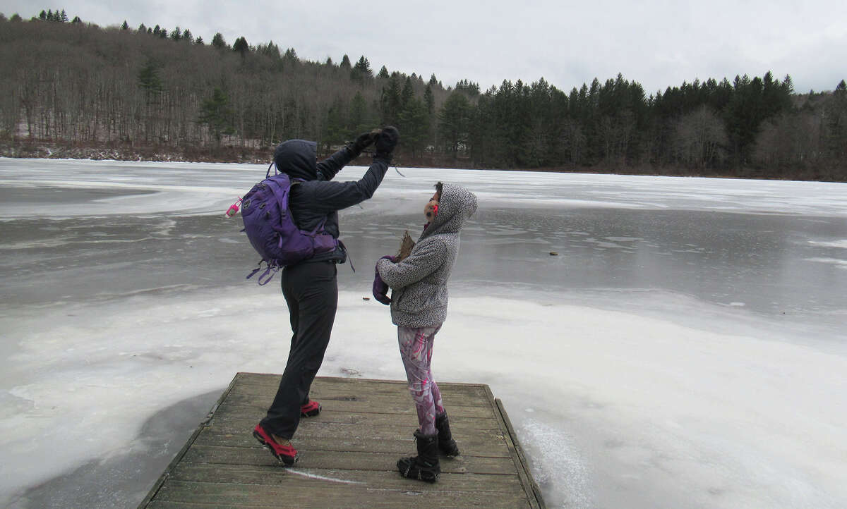 Gillian Scott tries to smash through the ice with a rock at White Birch Pond in the Partridge Run Wildlife Management Area.