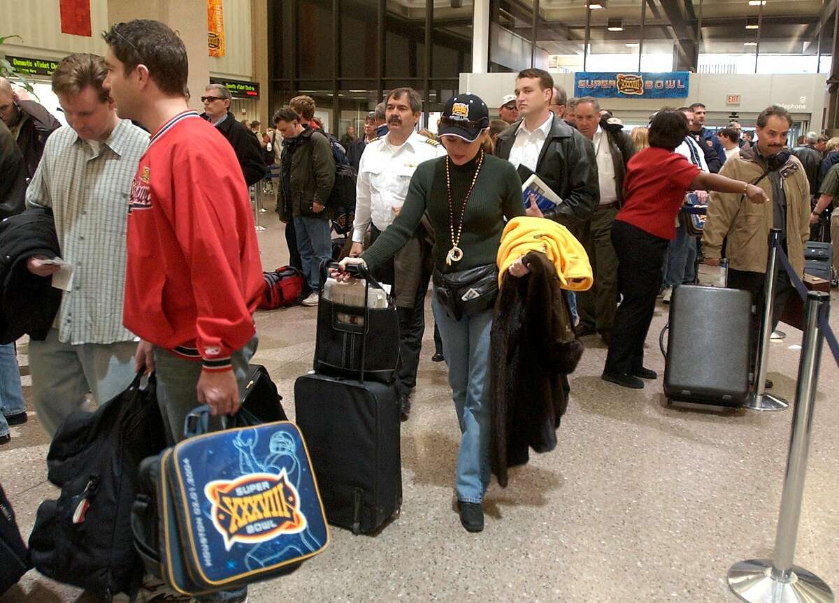 01/02/04--Steve Snyder, left, (red shirt) carries seat cushions through security lines at the airport and Karen Guise (center) wears her Suprebowl hat as they each prepare to leave Houston after attending the game. Snyder was returning home to San Diego, Calif. and Guise was continuing her vacation by going to Vale Colorado to Ski. (Note: they were not together) Passengers crowded Bush Intercontinental Airport as they return home from the Superbowl. Photo by Steve Campbell