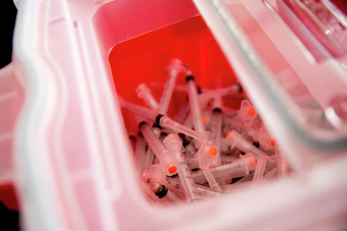 A container is filled with discarded needles that were used to give the first doses of the Moderna COVID-19 vaccine.