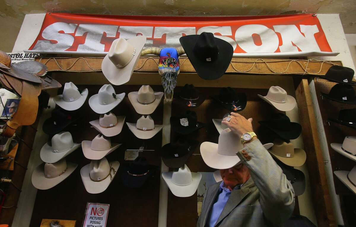 Paris Hatters owner Abe Cortez (right) puts on a hat at his store in 2017. The San Antonio business has hatted customers for more than 100 years.