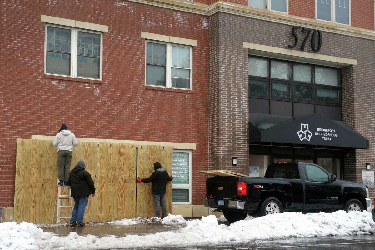 Workers put plywood into place to cover up damage caused when a vehicle crashed into the Gateway apartments following a two-car accident at the intersection of State St. and West Ave., in Bridgeport, Conn. Feb. 9, 2021.
