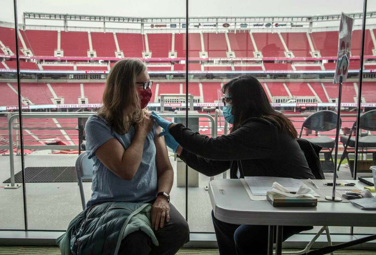 Clinical nurse Lynette Ancheta (right) checks Lynda Barbieri's arm before giving her the Pfizer COVID-19 vaccine at Levi’s Stadium in Santa Clara on Tuesda.