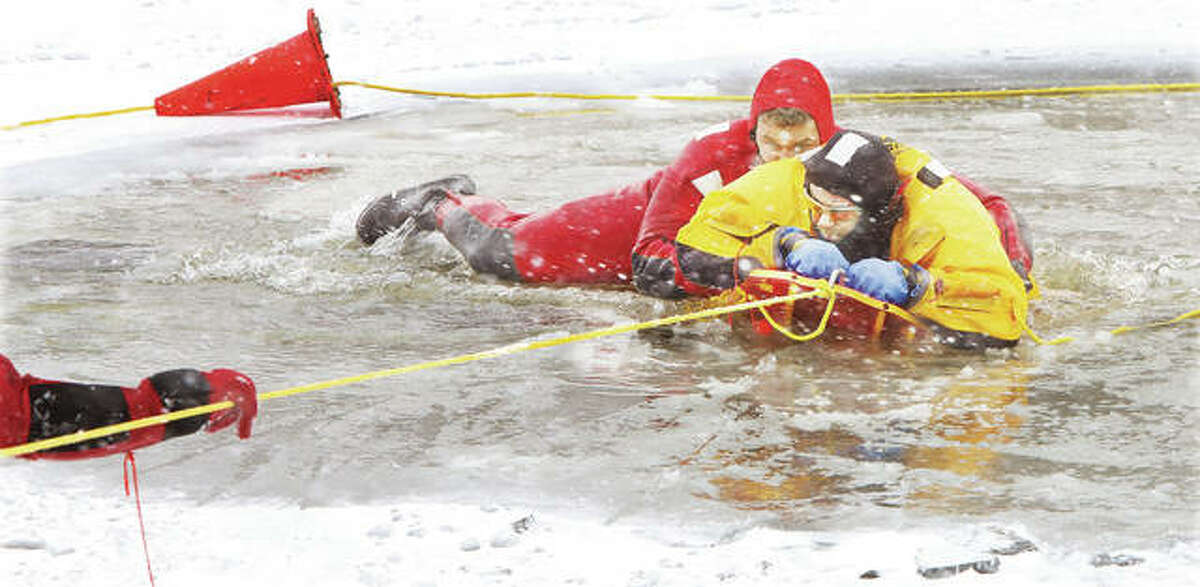 Alton Batallion Fire Chief Matthew Fischer, in yellow, is pulled to safety from the ice cold waters of the pond at the Olin T. Spencer Golf Course where Alton firefighters have been practicing ice training. Firefighters took advantage of the frigid weather to do the training not possible in recent years due to mild winters. Fischer, who doubled as both instructor and mock victim, was pulled out of the water on a specialized sled used for ice rescues by firefighters wearing protective wetsuits.