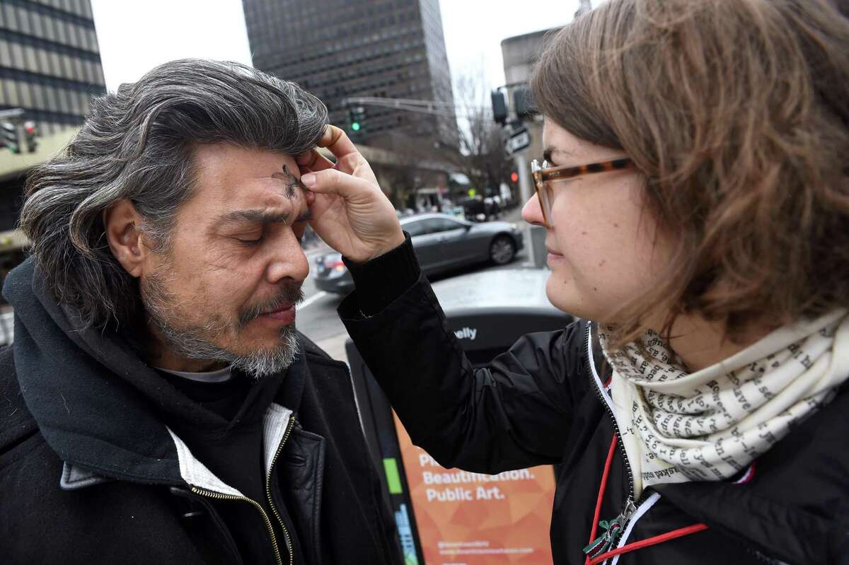 Heidi Thorsen (right), outreach coordinator for Trinity on the Green, applies ashes to the forehead of Angel Roman of New Haven for Ash Wednesday in front of the church on the New Haven Green on February 26, 2020. Because of the COVID-19 pandemic, this year priests will either sprinkle ashes on people’s heads or use a cotton swab to apply them.
