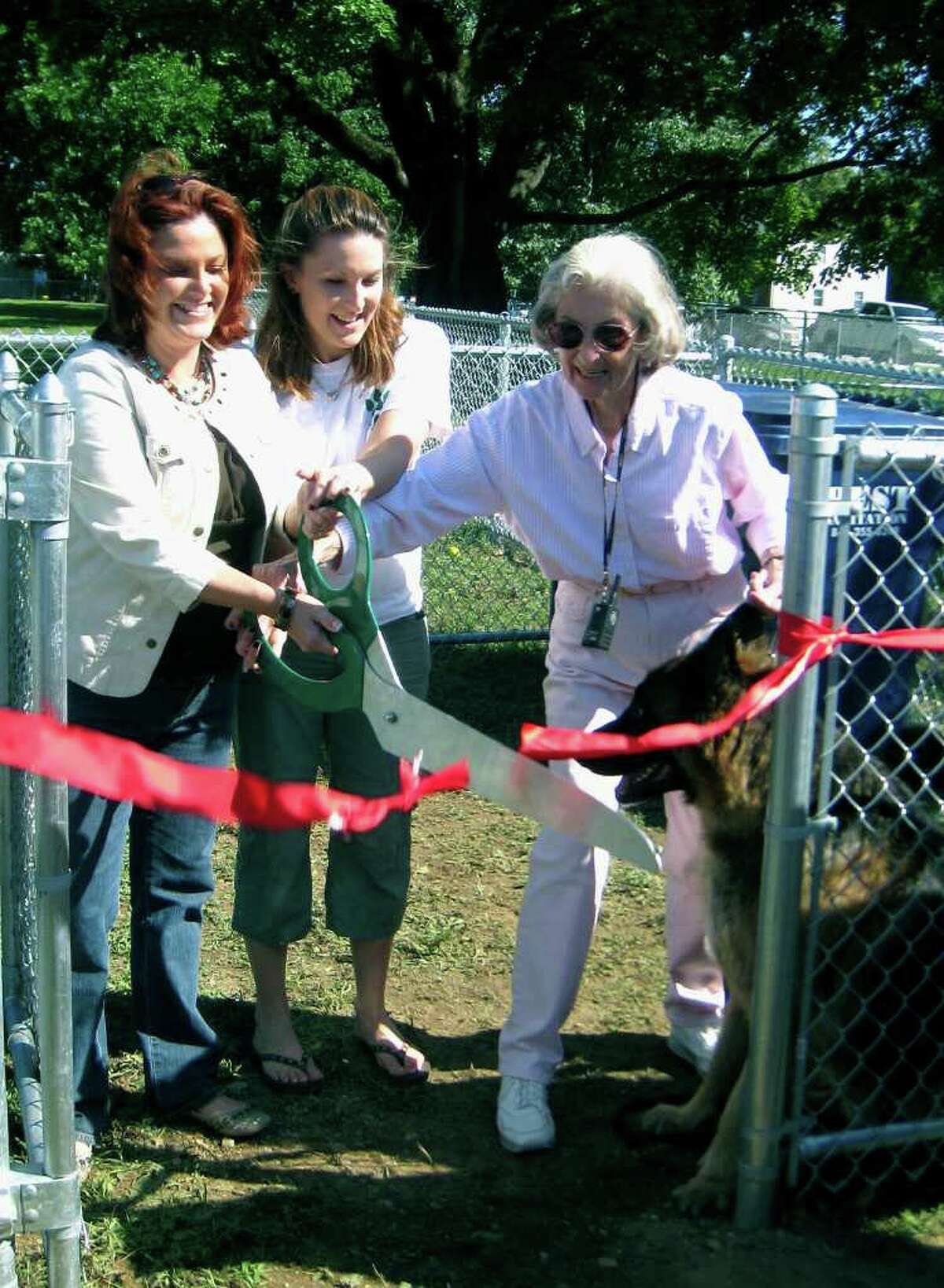 SPECTRUM/Performing the ribbon-cutting at the Aug. 28, 2010 opening of the town's Candlewoof! dog park along Pickett District Road in New Milford are, from left to right, New Miolford mayoral administrative aide Tammy Reardon, her sister, Lori Sartwell, who serves as the dog park committee president, and Frances Terry, whose family donated the fencing for the park in memory of her husband, Norman Terry. Looking on with great interest is Mrs. Terry's dog, Jake.
