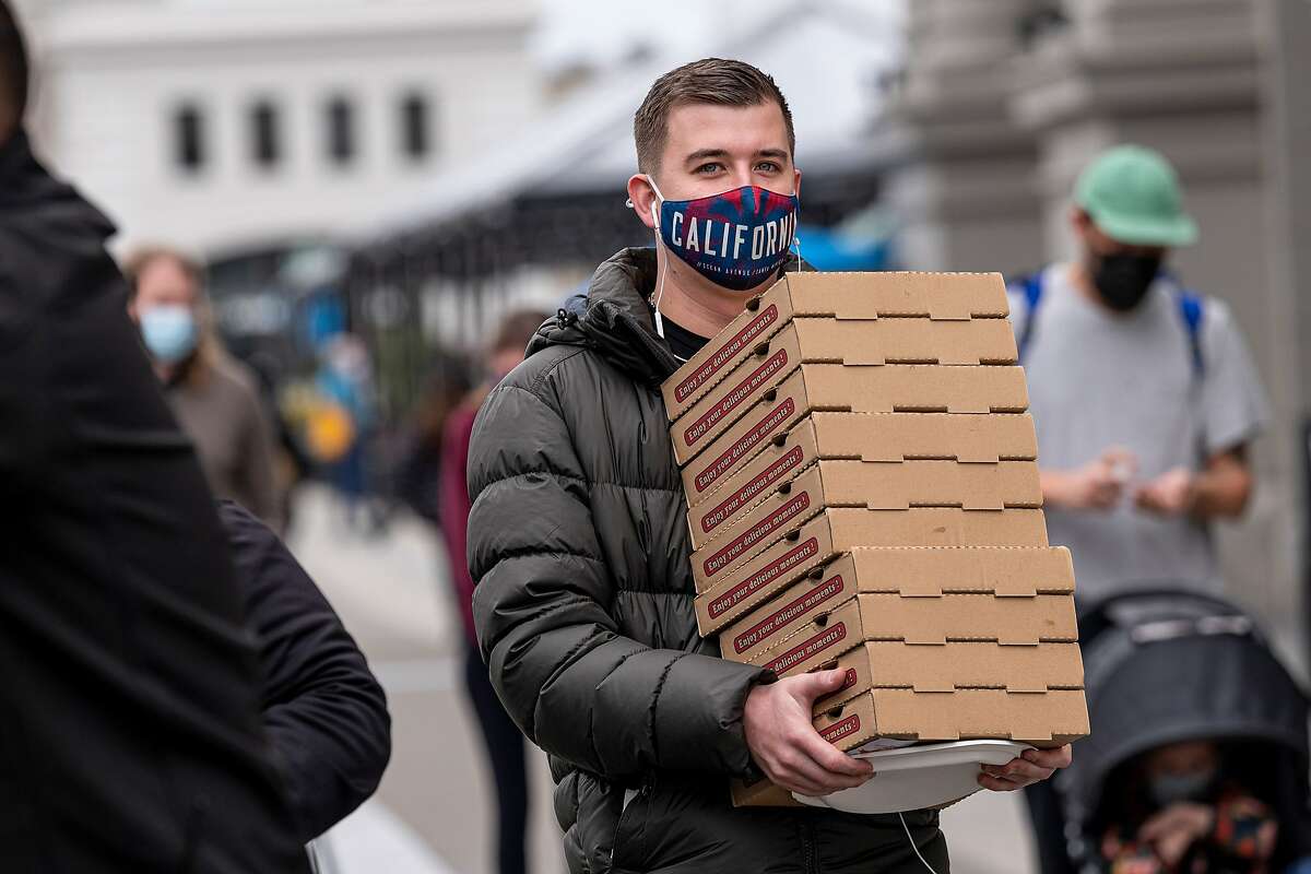 A person wearing a protective mask carries pizza boxes on The Embarcadero in San Francisco, California, U.S., on Thursday, Feb. 11, 2021. The U.S. Centers for Disease Control and Prevention Wednesday began recommending that Americans wear a cloth mask over a medical mask to slow the spread of Covid-19, along with other options to improve mask fit. Photographer: David Paul Morris/Bloomberg