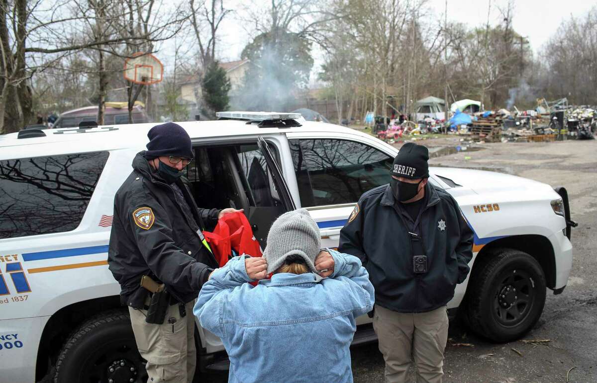Harris County Deputy Sheriffs James Kelley, left, and Jason Dean, give a woman a beanie ahead of a winter storm Saturday, Feb. 13, 2021, in Harris County. The woman and several others lived in the lot, and the Homeless Outreach Team handed out cold-weather items and offered assistance.