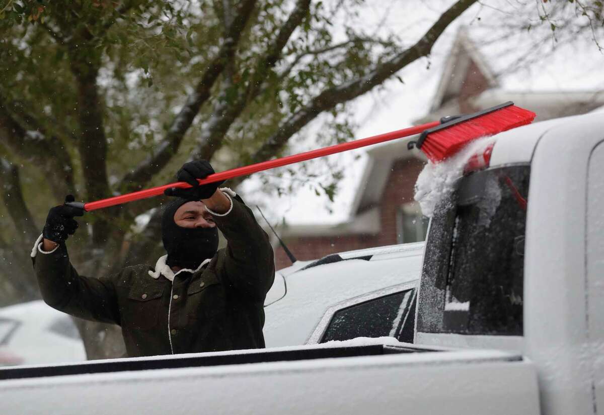 Patrick Minott uses a push broom to scrape snow and ice covered off his vehicles, Monday, Feb. 15, 2021, in Kingwood.