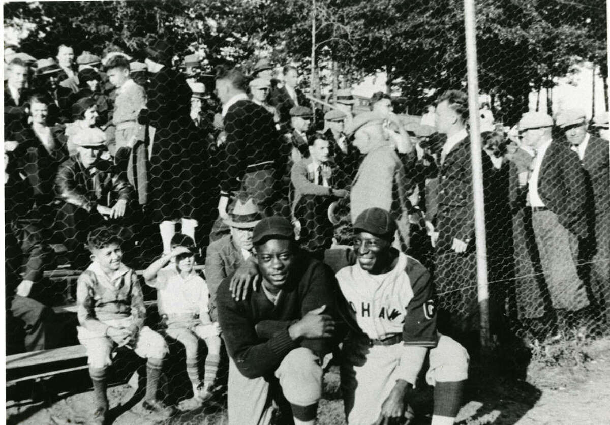 Two unidentified Mohawk Giants players, possibly pitcher Adolph Fleming and infielder Marcel Brooks, standing in front of the bleachers at Central Park in Schenectady, New York as the crowd fills them.
