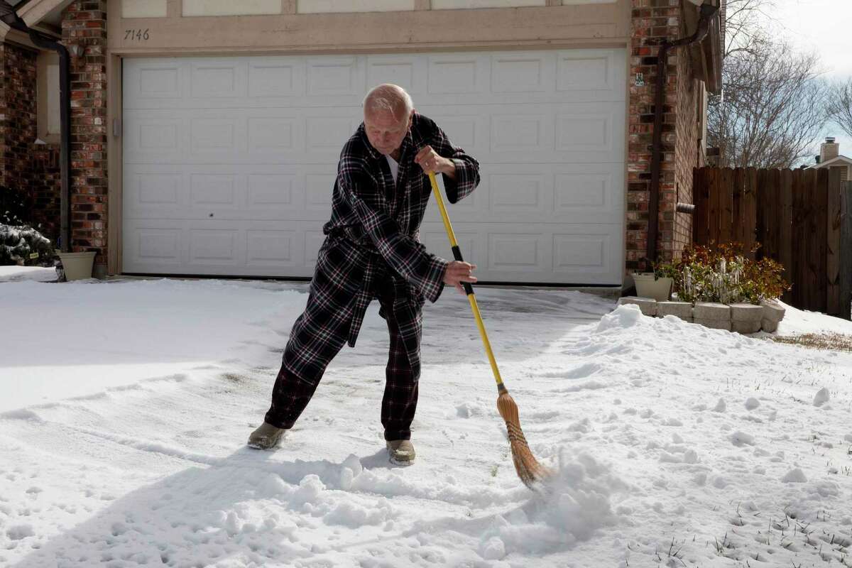 Art Liming brushes his the snow off his driveway on the Northeast Side with a broom on Tuesday. Liming’s power went out that morning and his water has been working intermittently.