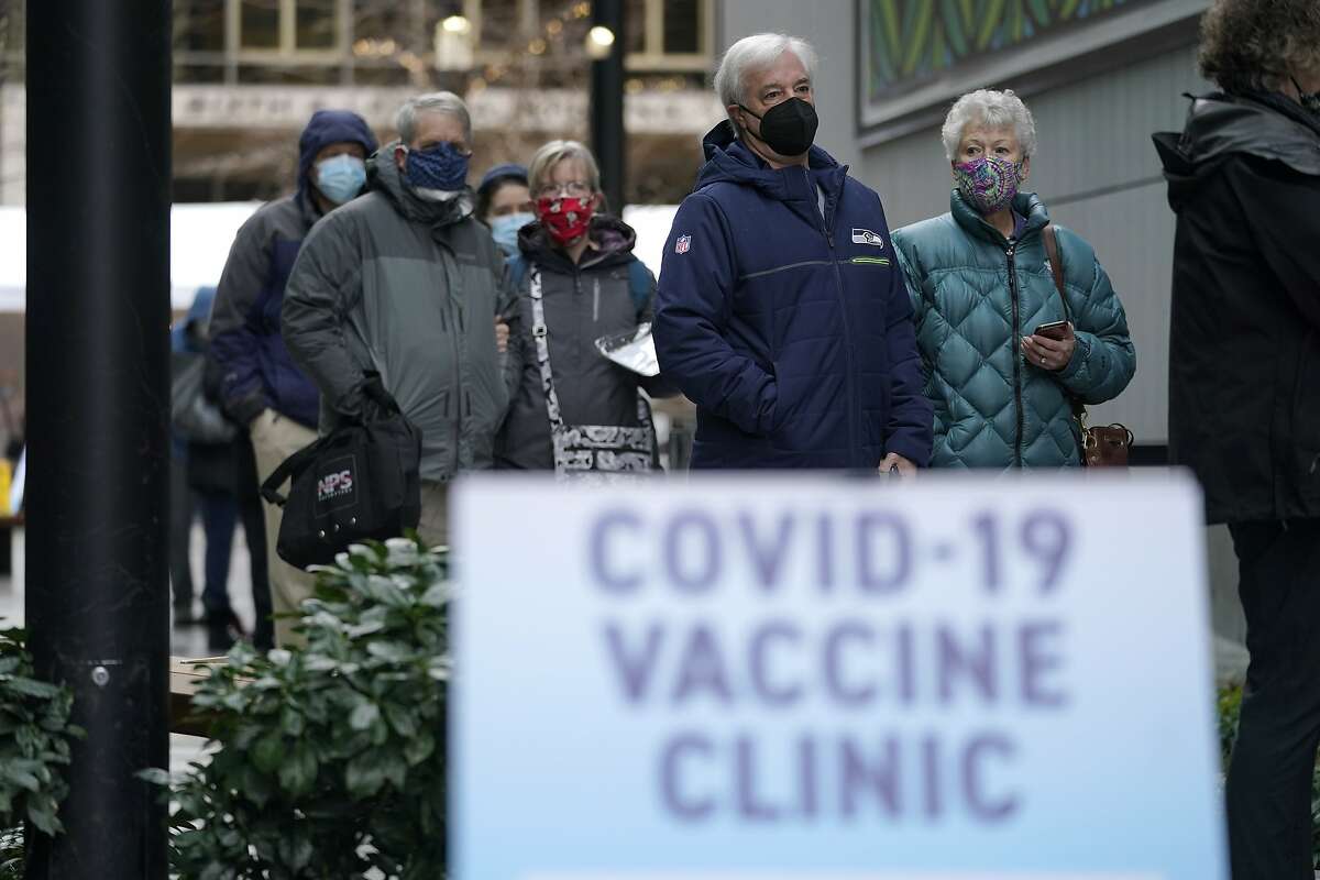 FILE - In this Jan. 24, 2021, file photo, people stand near a sign as they wait in line to receive the first of two doses of the Pfizer vaccine for COVID-19, at a one-day vaccination clinic set up in an Amazon.com facility in Seattle and operated by Virginia Mason Franciscan Health. (AP Photo/Ted S. Warren, File)