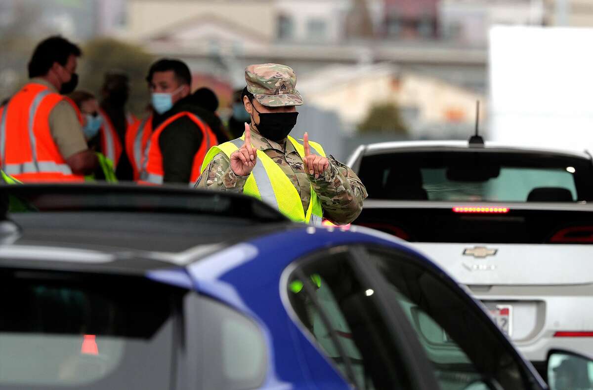 A California National Guard member signals a driver to wait at the Coliseum mass vacination site on Tuesday.