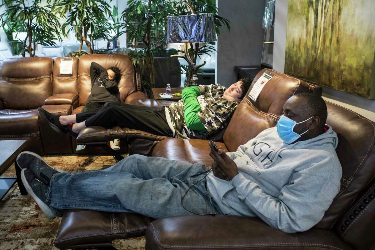 Russell Johnson sits on a recliner as he sits with his son, Jaleel, far left, and Shawn Blanc at a warming shelter set up at Gallery Furniture Tuesday, Feb. 16, 2021 in Houston. As emperatures stayed below freezing Tuesday, and many in the neighborhood around the furniture store without power, Jim
