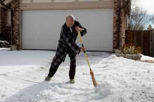 Art Liming brushes his the snow off his driveway in Northeast San Antonio with a broom on Feb. 16, 2021. Liming’s power went out Tuesday morning and his water has been working intermittently.