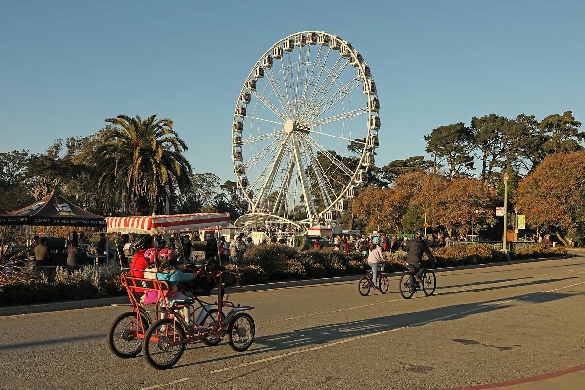 Bikers pass a long line of people for the SkyStar Observation Wheel Golden Gate Park, Saturday, Nov. 28, 2020, in San Francisco, Calif.