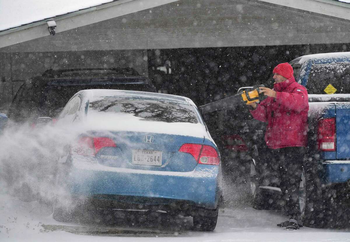 Saul Cortez uses a leaf blower to remove snow from his car on Thursday morning.