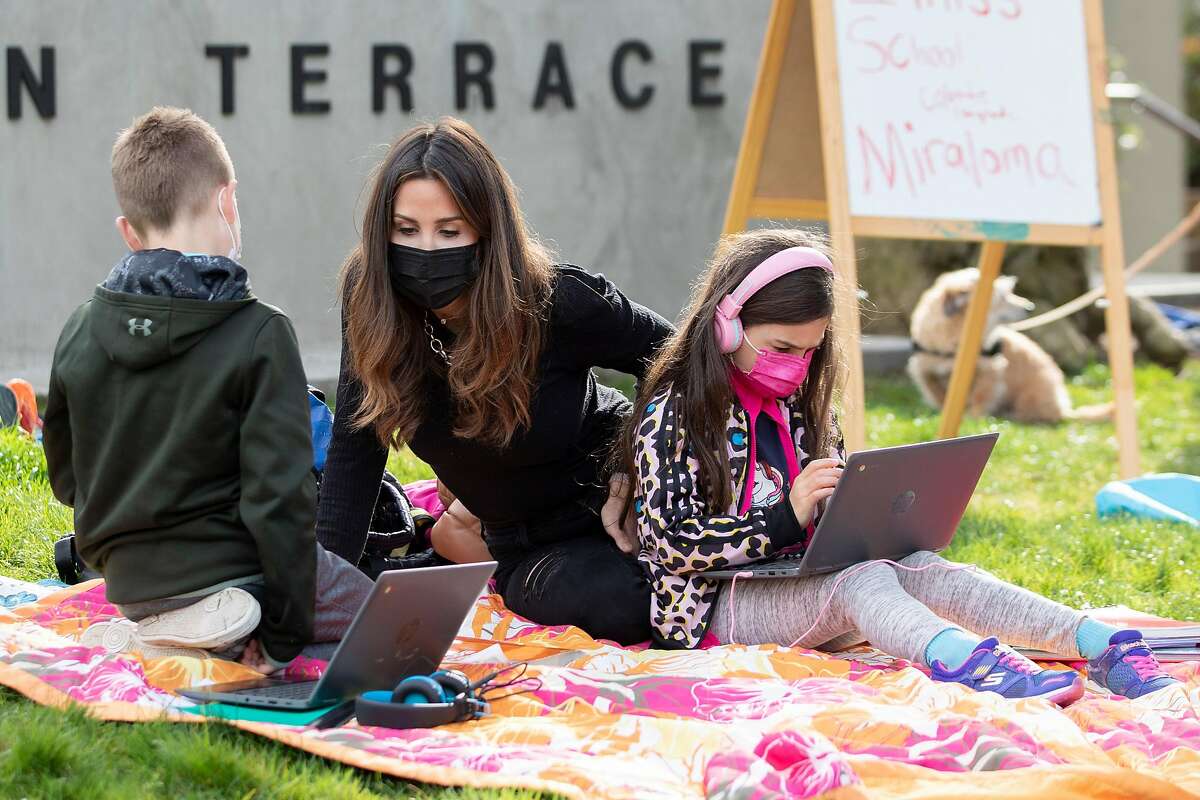 Sarah Swanson (center) helps her son, Hayes, 9, and daughter Larkin, 7, with their class connection while gathered with fellow students at Midtown Terrace Park across the street from Clarendon Elementary School in San Francisco, Calif. Thursday, February 18, 2021 to participate in a “Zoom in” demonstration with fellow students attending classes outside their schools to bring attention to reopening.