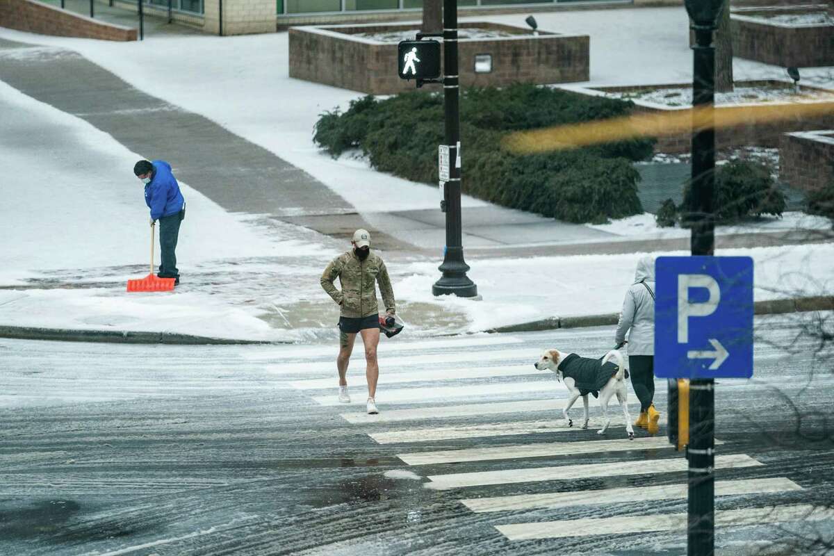 A man shovels a sidewalk as a pedestrian walks along Wilson Blvd. in Arlington, Va., Feb. 18, 2021.