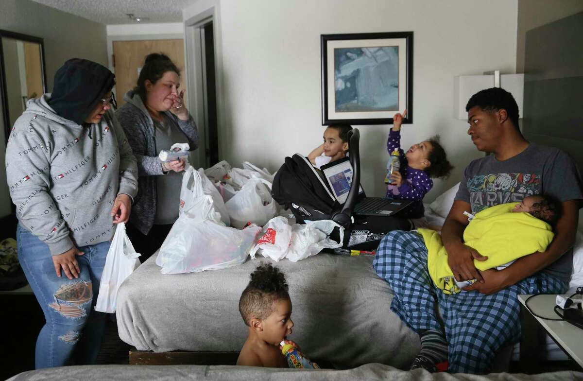 Brandy Robinson, 36, second from left, brings groceries to her family taking refuge at the Best Western Hotel off Loop 410 on Feb. 18, 2021. Their Seven Oaks Apartment unit flooded when a pipe leading to the water heater burst on Monday. With her are her daughter, Cierra Arceneaux, 18, left, and the daughter’s boyfriend, Marquez Holmes, 18, right, holding their 2-month-old son, Legend. The couple’s first born, Da’Mir Holmes, 2, plays between the beds. In the background are Robinson’s son, Moses Delagarza, 1, and Addilynn Houston, 1, whose mother is also staying with them in the room.