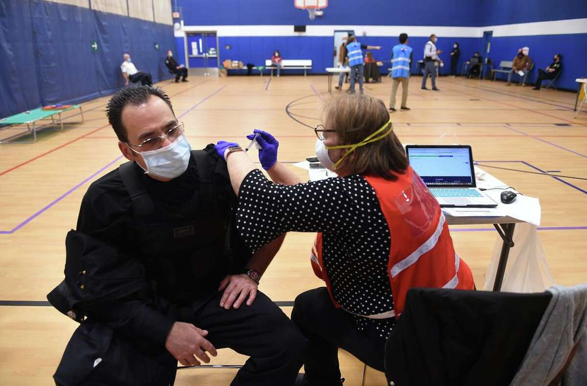 Madison Police Officer John Palmer (left) gets a dose of the Moderna COVID-19 vaccine by RN Maureen Spinnato at the Madison Town Campus gymnasium on Jan. 6, 2021.