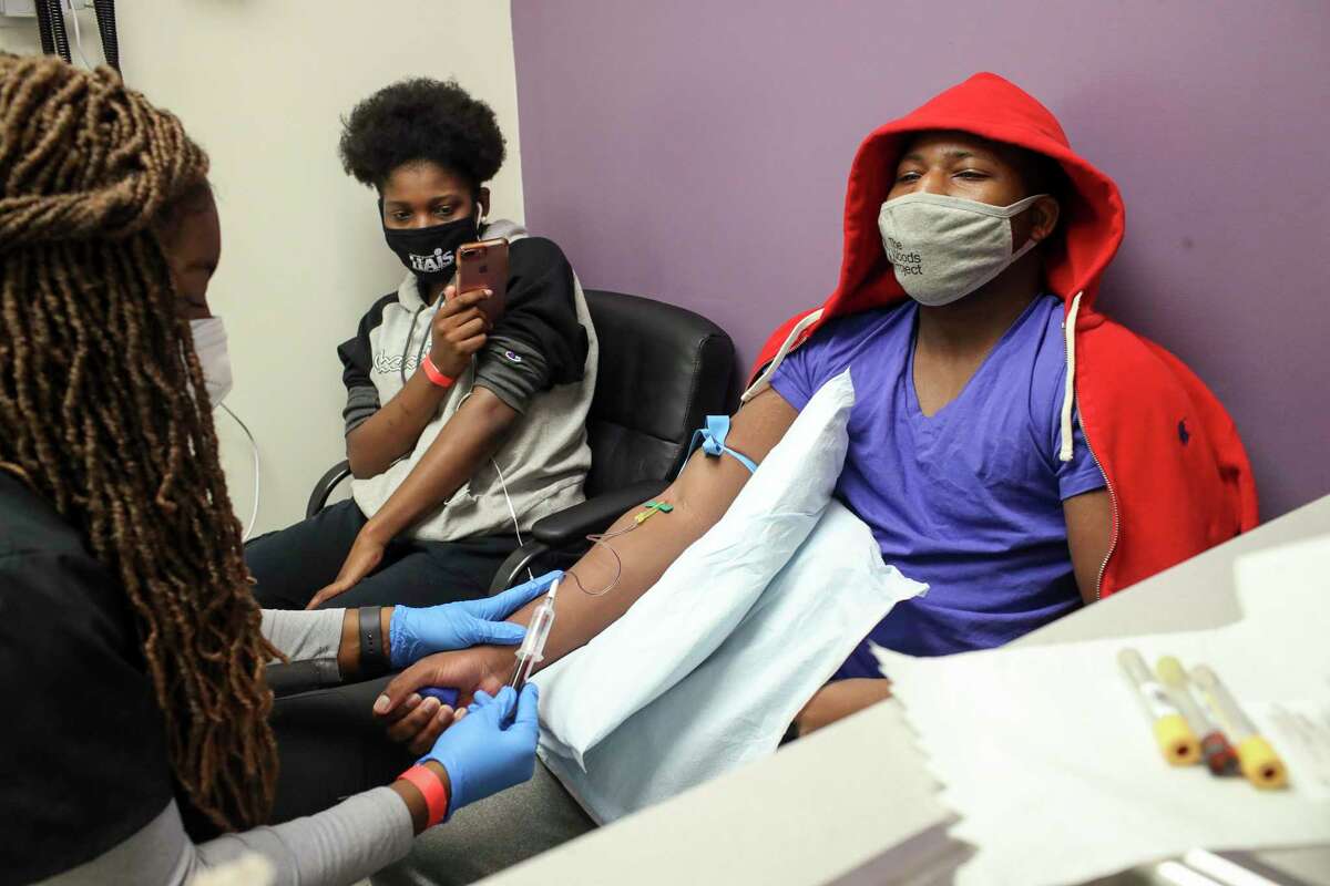 Animi Williams, 14, center, laughs as her brother Adonye Williams, 16, has his blood drawn by Tenea Johnson, a research assistant, as part of a Moderna vaccine trial for teenagers Saturday, Feb. 13, 2021, at CyFair Clinical Research Center in Houston. Animi Williams was live-streaming the blood draw for their mother, who was waiting outside in their car.